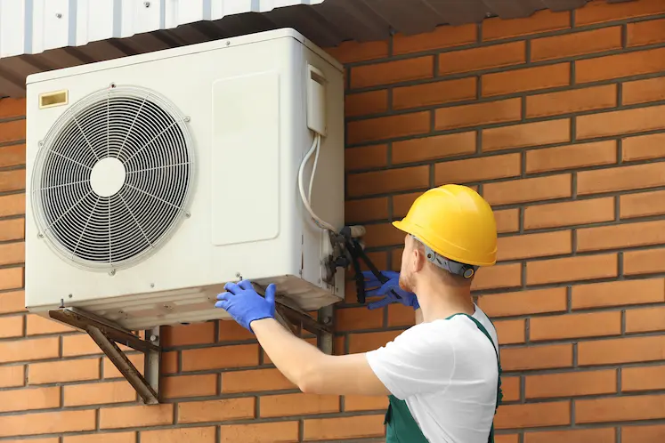 tecnico ripara condizionatore installato su edificio in mattoni in Friuli Venezia Giulia